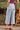 A woman wearing light wash “Ab”solution® wide leg jeans and a tucked-in top, seen from behind, standing on a stone path outdoors.